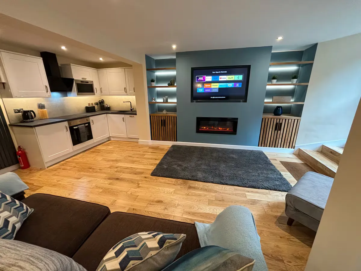 The open-plan living room at Minster Bells Suite, with a media wall, electric fire and modern kitchen