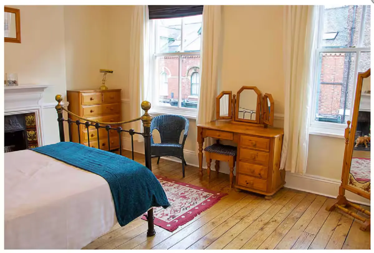 A characterful double bedroom with a cast-iron bed frame, original fireplace and pine dressing table